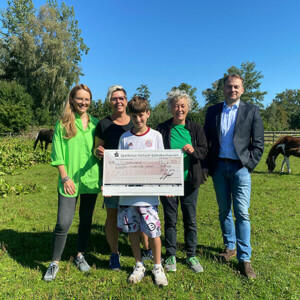 Auf dem Bild sieht man 2 Frauen, einen Mann und einen Jungen, der einen großen Scheck in der Hand hält