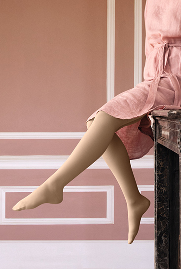 2. Immagine Lifestyle Juzo Soft  Donna con Juzo Soft Sesame seduta su una mensola del camino