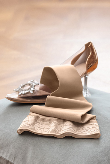 3. Immagine Lifestyle Juzo Soft  Juzo Soft Sesame disteso su un cuscino accanto a una scarpetta di Cenerentola