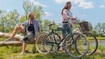 A man and a woman on a bicycle by the lake. The man is wearing a knee support..