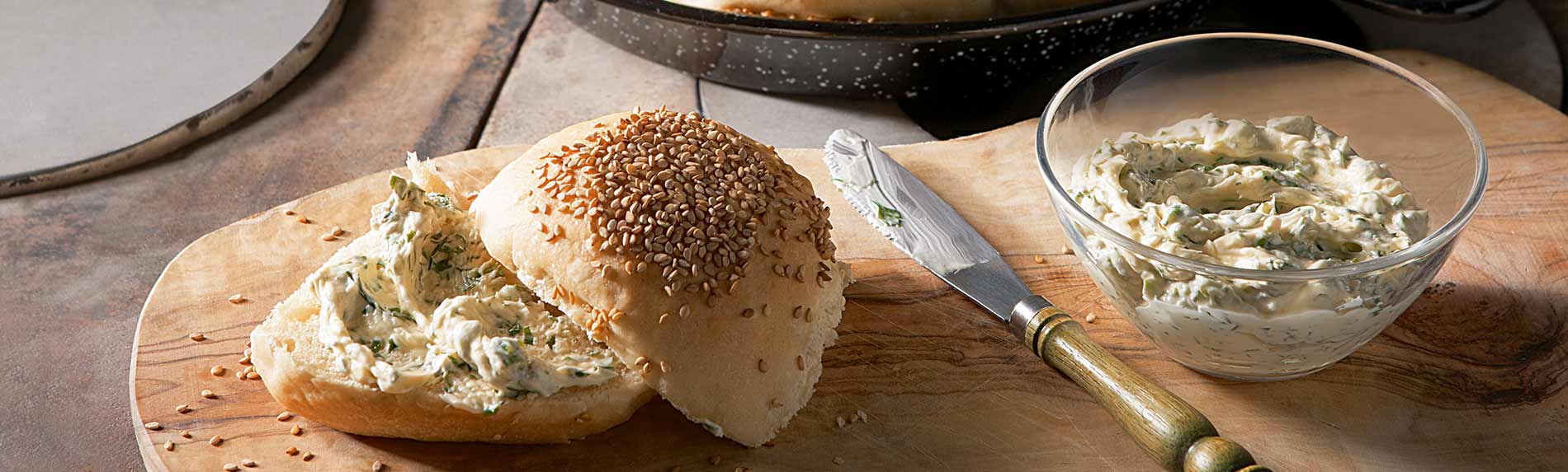 Sesam-Pfannenbrötchen mit Kräuterbutter Sesam Pfannenbrötchen mit Kräuterbutter auf einem Holzbrett