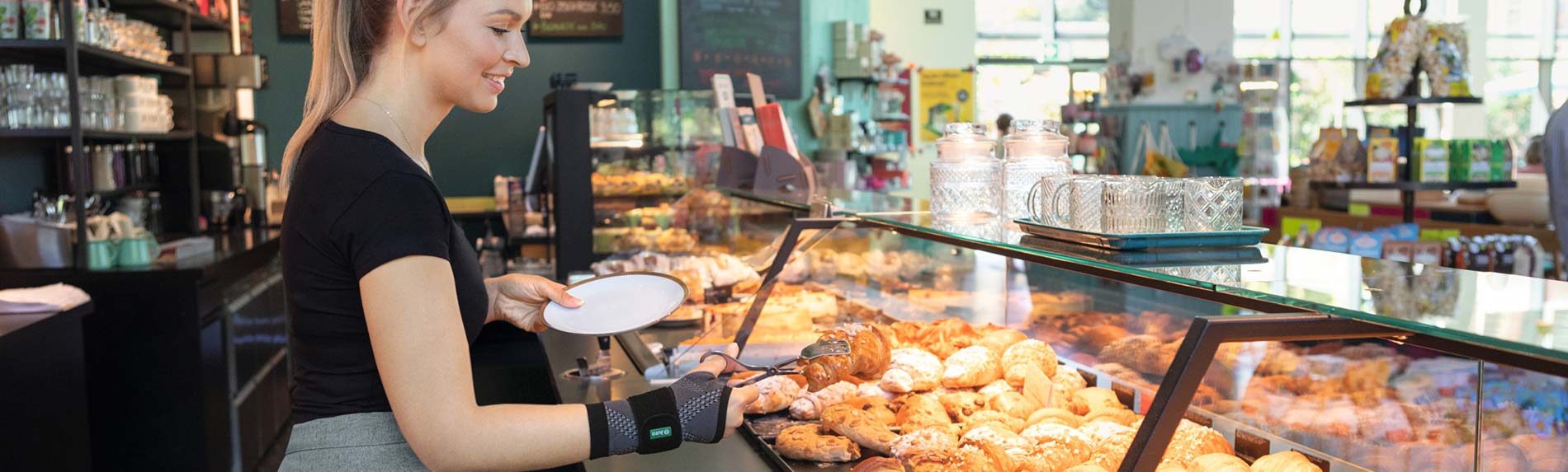 Bakery employee wearing a JuzoFlex Manu Xtra wrist support grabs a croissant with serving tongs