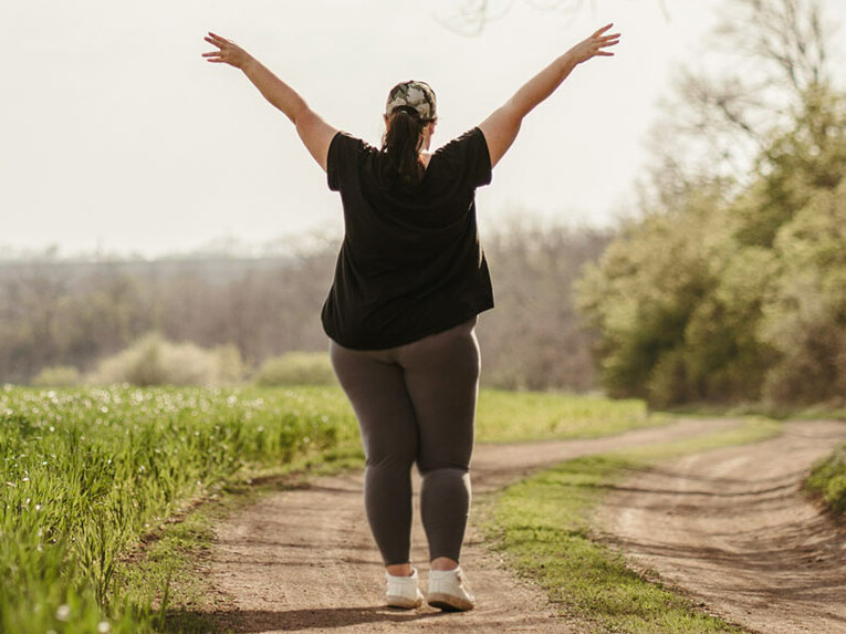Eine Frau mit etwas mehr Gewicht ist in Sportsachen auf einem Feldweg unterwegs