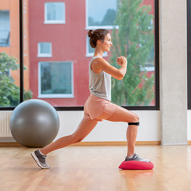 A woman doing a lunge forwards on a soft cushion