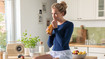 A woman is sitting on the kitchen counter drinking orange juice. She is wearing a compression chest support