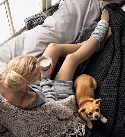 Eine Frau sitzt in eine Decke gekuschelt auf der Couch und trinkt einen Kakao Eine Frau sitzt in eine Decke gekuschelt auf der Couch und trinkt einen Kakao